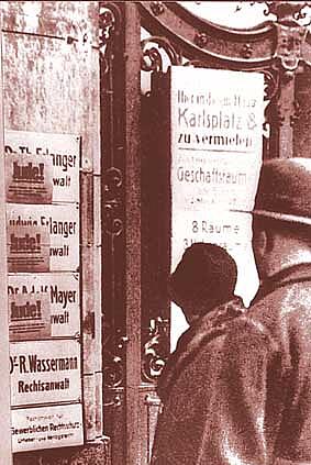 Ein Paar schauen am 1. April 1933 auf rote Handzettel, die auf Kanzleischilder geklebt wurden.  Plakaten geklebt sind. SA-Posten fordern: „Geht nicht zu jüdischen Rechtsanwälten“; an die Kanzleischilder wurden rote Handzettel geklebt: „Besuch verboten! Jude!“